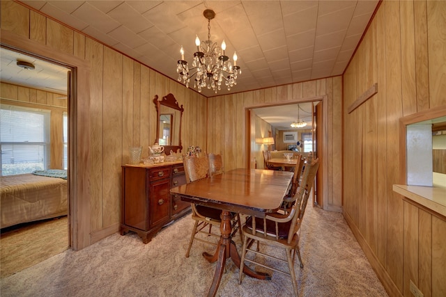 dining room with wooden walls, a notable chandelier, and light colored carpet