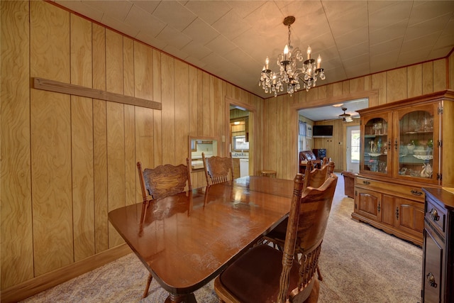 dining area featuring light colored carpet, wood walls, and ceiling fan with notable chandelier