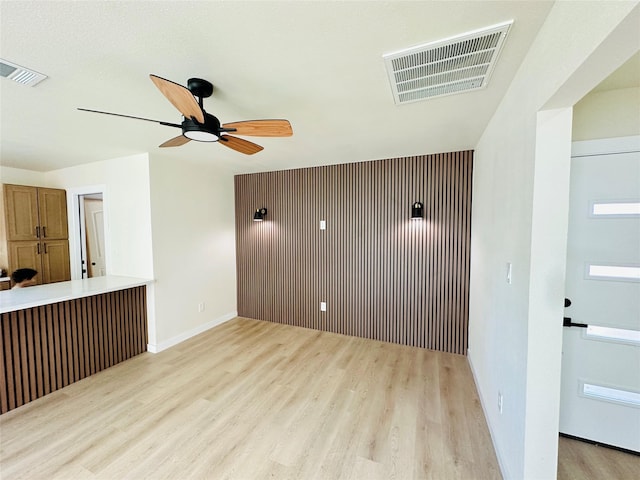 empty room featuring light wood-type flooring, a ceiling fan, and baseboards