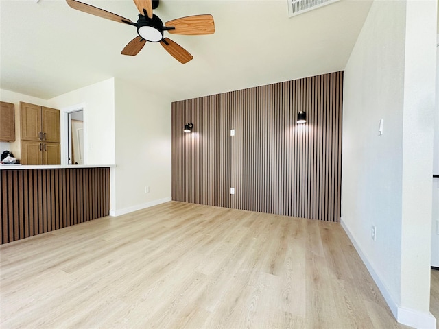 empty room featuring light wood finished floors, a ceiling fan, and baseboards