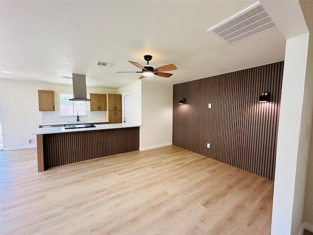 kitchen with island exhaust hood, light wood-type flooring, a peninsula, ceiling fan, and light countertops