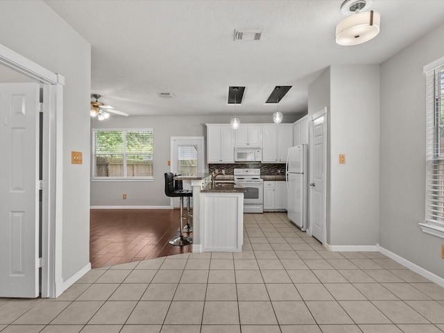 kitchen featuring dark countertops, white appliances, a breakfast bar area, white cabinets, and baseboards
