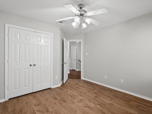 unfurnished bedroom with wood finished floors, visible vents, a closet, baseboards, and ceiling fan