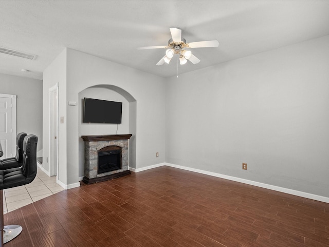 unfurnished living room featuring wood finished floors, a stone fireplace, ceiling fan, baseboards, and visible vents