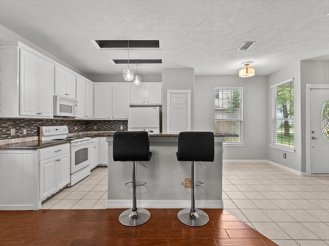 kitchen with a kitchen bar, decorative backsplash, white cabinetry, and white appliances