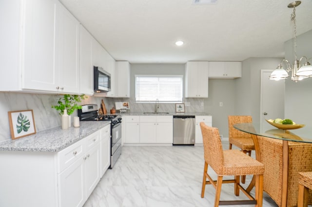 kitchen featuring light stone counters, a sink, a chandelier, white cabinets, and appliances with stainless steel finishes