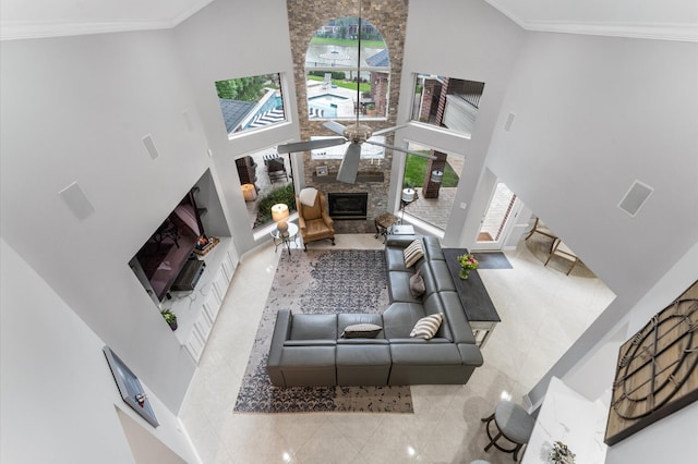 tiled living area with a stone fireplace, a ceiling fan, a high ceiling, and ornamental molding