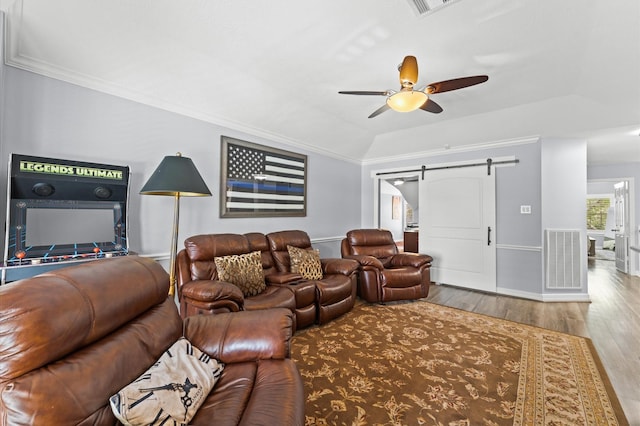 living room featuring ceiling fan, visible vents, crown molding, wood finished floors, and a barn door