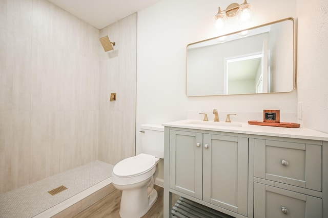 full bathroom featuring toilet, wood finished floors, vanity, and tiled shower