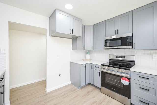 kitchen featuring light wood finished floors, decorative backsplash, appliances with stainless steel finishes, and gray cabinets