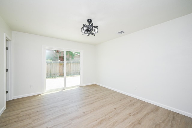 empty room featuring baseboards, a chandelier, light wood-style floors, and visible vents