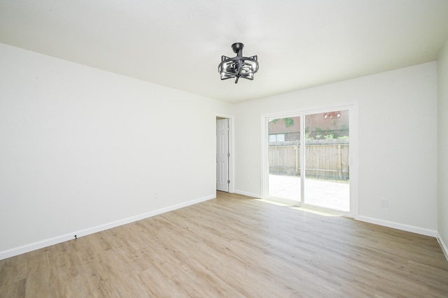 empty room featuring wood finished floors, baseboards, and an inviting chandelier