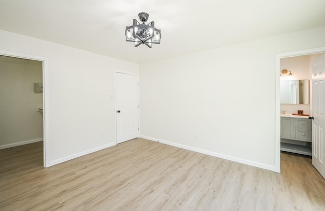 unfurnished bedroom featuring ensuite bathroom, a closet, a spacious closet, light wood finished floors, and baseboards