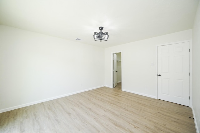unfurnished room featuring a chandelier, light wood-style flooring, visible vents, and baseboards