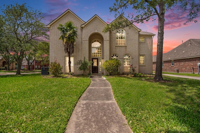 french country style house with central AC unit, brick siding, and a front yard