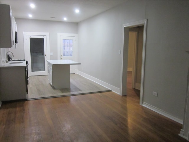 kitchen with recessed lighting, wood finished floors, a sink, a kitchen island, and baseboards