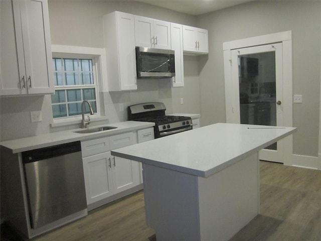 kitchen featuring light countertops, wood finished floors, a sink, appliances with stainless steel finishes, and white cabinetry