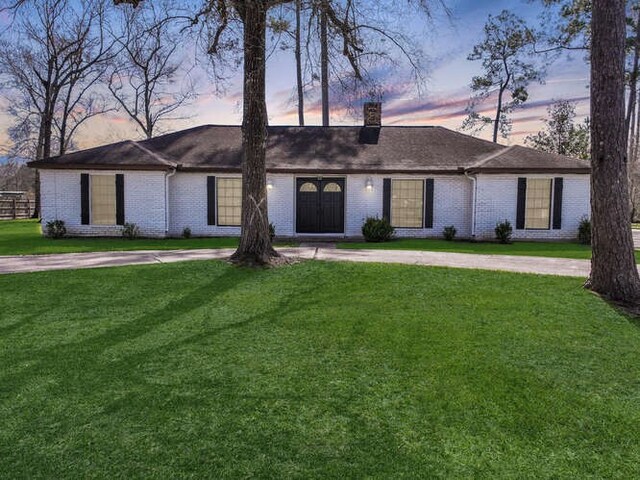 ranch-style house featuring a chimney, a front lawn, brick siding, and curved driveway