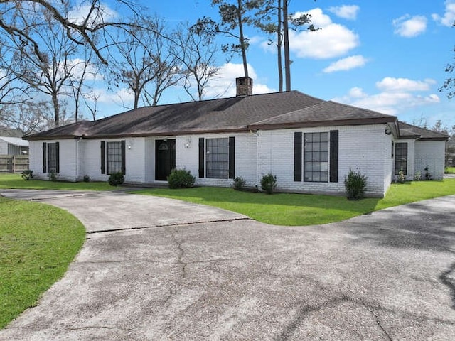 ranch-style house featuring a front lawn, driveway, a chimney, and brick siding