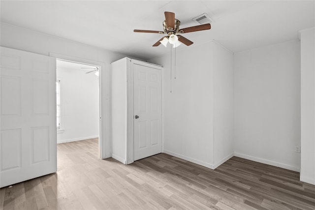 interior space with baseboards, a ceiling fan, visible vents, and light wood-type flooring