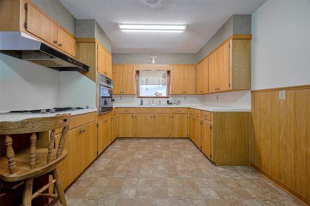 kitchen with oven, a sink, stone finish floor, light countertops, and under cabinet range hood
