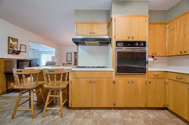 kitchen with under cabinet range hood, light countertops, white gas stovetop, black oven, and stone finish flooring