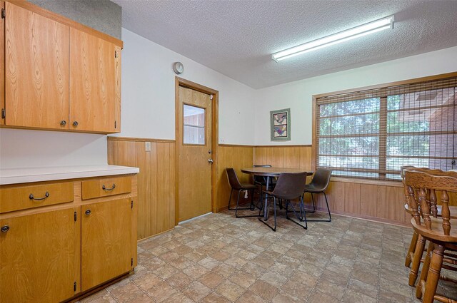 dining space with a wainscoted wall, wood walls, a textured ceiling, and stone finish flooring