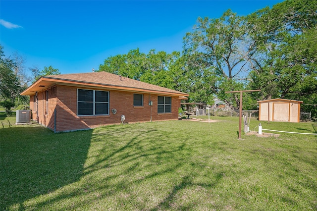 back of house with central air condition unit, a lawn, an outdoor structure, brick siding, and a storage unit