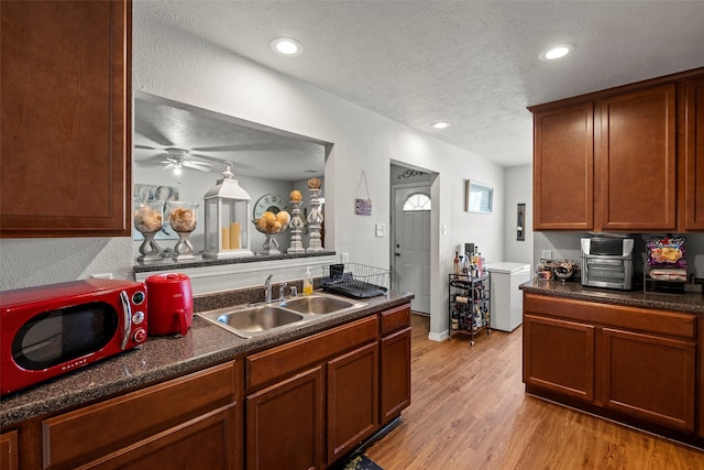 kitchen with light wood-type flooring, dark countertops, a sink, and a textured ceiling