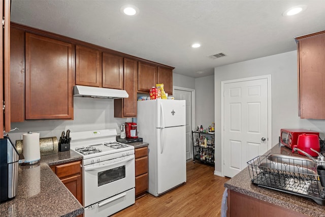 kitchen featuring dark countertops, white appliances, light wood finished floors, under cabinet range hood, and visible vents