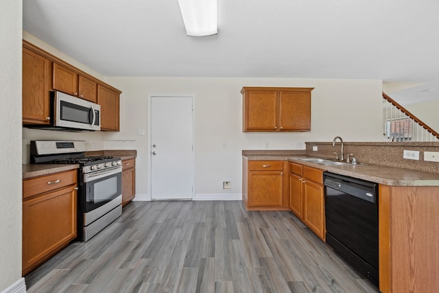 kitchen featuring brown cabinets, light wood finished floors, a sink, and appliances with stainless steel finishes