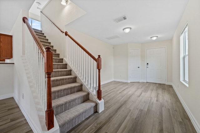 foyer entrance with baseboards, visible vents, wood finished floors, and stairs