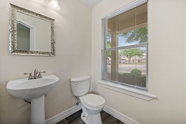 half bath featuring a sink, wood finished floors, toilet, and baseboards