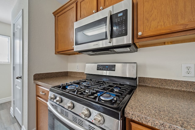 kitchen with baseboards, brown cabinetry, stainless steel appliances, and tile counters