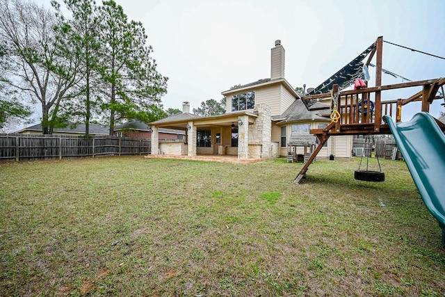 rear view of house with stone siding, a playground, a chimney, a yard, and a fenced backyard