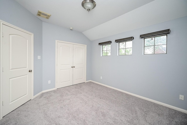 unfurnished bedroom with a closet, carpet flooring, baseboards, visible vents, and lofted ceiling