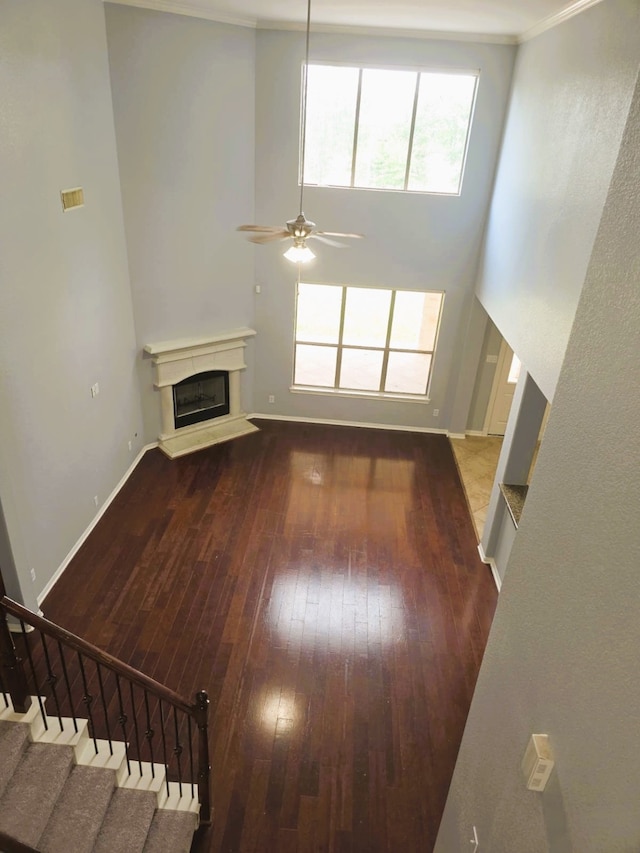 unfurnished living room with crown molding, ceiling fan, hardwood / wood-style floors, baseboards, and a glass covered fireplace