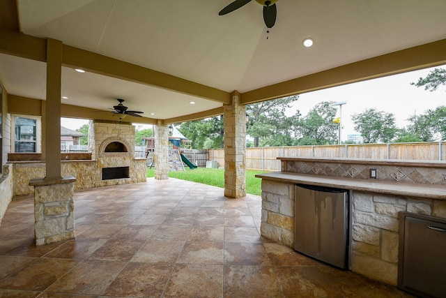 1106 Windsor Chase Ln, Spring, TX 77373 - view of patio / terrace with an outdoor stone fireplace, a ceiling fan, a fenced backyard, exterior kitchen, and a playground