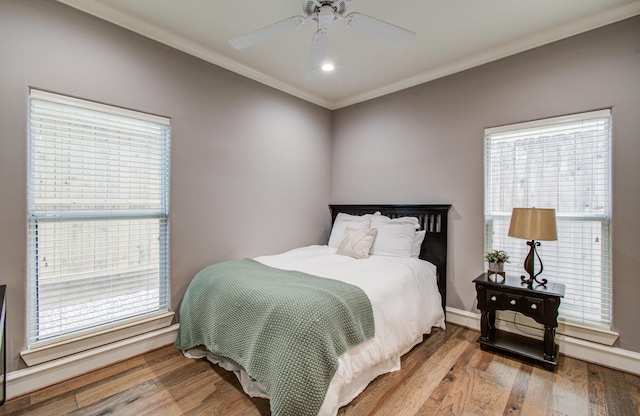 bedroom with multiple windows, baseboards, crown molding, and wood finished floors