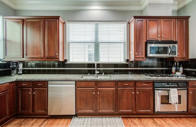 kitchen featuring light wood finished floors, a sink, decorative backsplash, appliances with stainless steel finishes, and ornamental molding