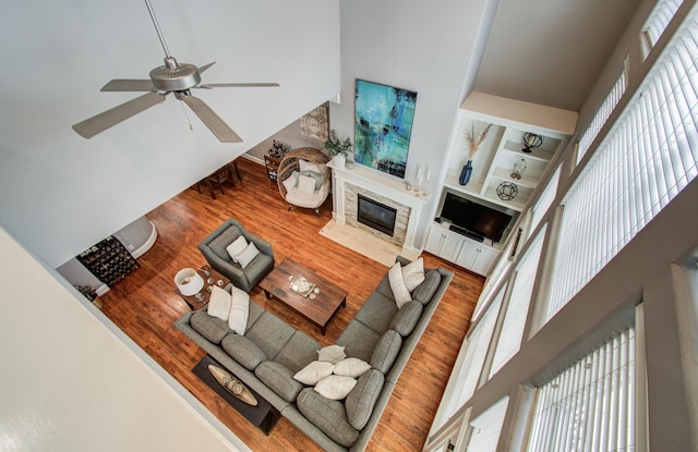 living area with a high ceiling, a high end fireplace, wood finished floors, a ceiling fan, and built in features