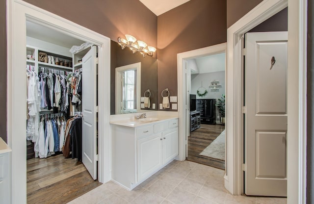 bathroom with a spacious closet, an inviting chandelier, vanity, and wood finished floors