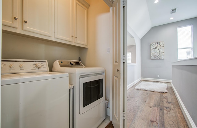 laundry area featuring wood finished floors, visible vents, washing machine and dryer, baseboards, and cabinet space