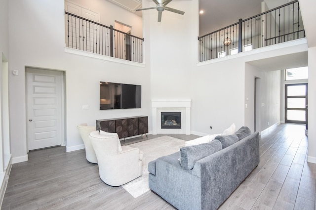 living area with a towering ceiling, wood finished floors, baseboards, a glass covered fireplace, and ceiling fan