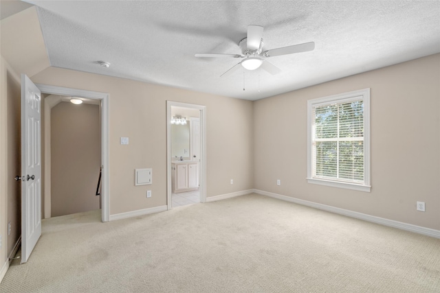 unfurnished bedroom with light colored carpet, a textured ceiling, ensuite bathroom, baseboards, and a ceiling fan