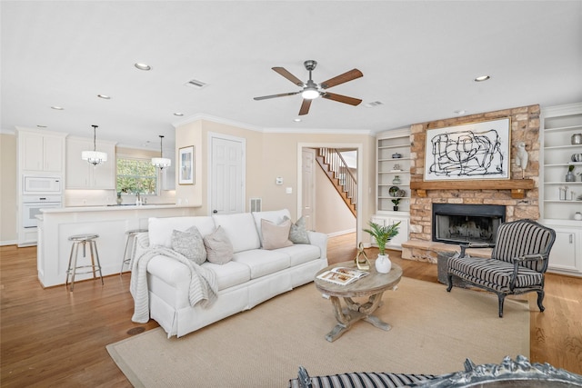 living room with light wood-style floors, a fireplace, ceiling fan, crown molding, and recessed lighting