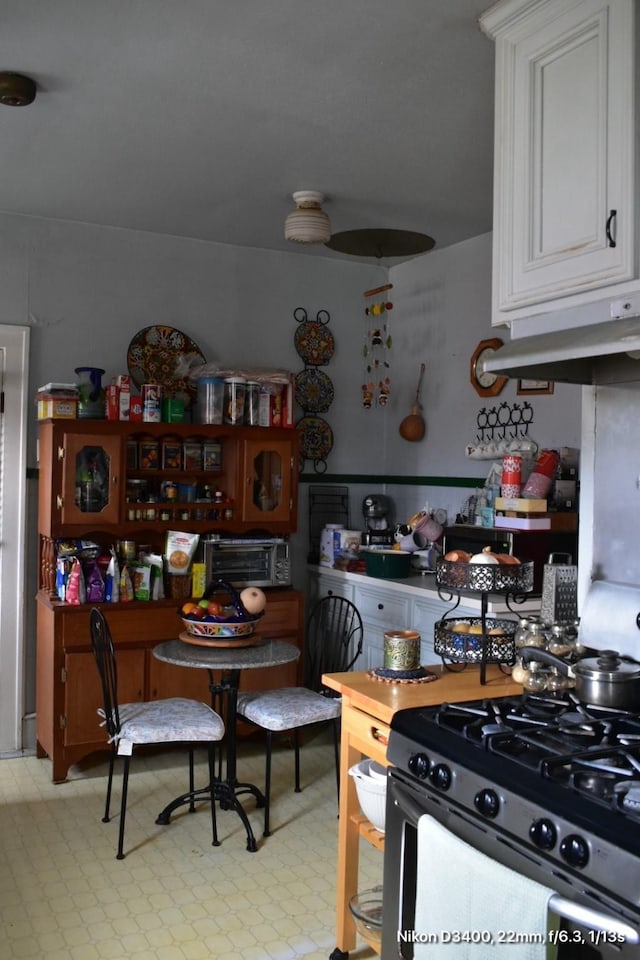 kitchen featuring stainless steel range with gas cooktop, white cabinetry, a toaster, and under cabinet range hood