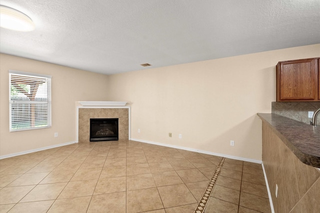 unfurnished living room featuring light tile patterned flooring, a textured ceiling, a tiled fireplace, and visible vents