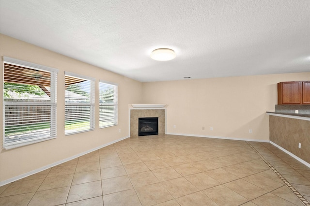 unfurnished living room with baseboards, light tile patterned flooring, a tile fireplace, and a textured ceiling