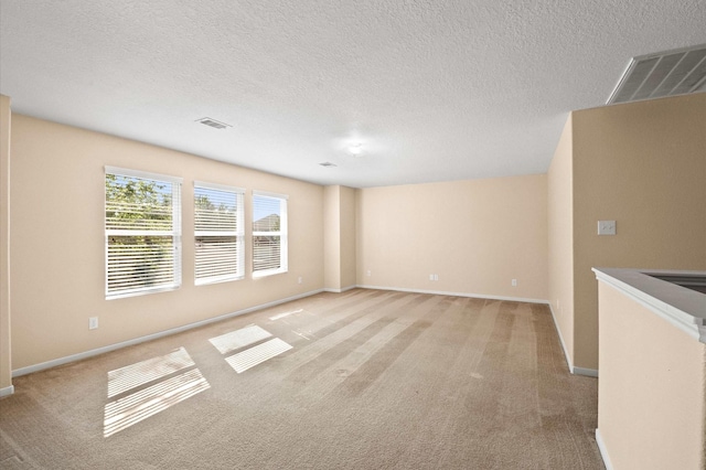 empty room with light carpet, baseboards, and a textured ceiling